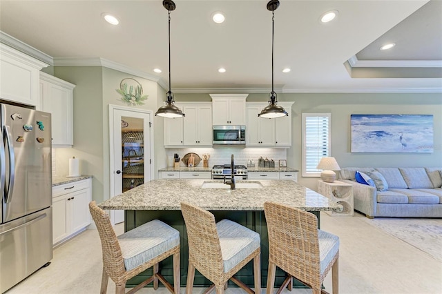 kitchen with an island with sink, appliances with stainless steel finishes, white cabinets, and pendant lighting