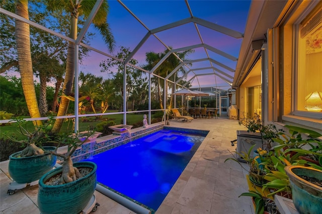 pool at dusk with a patio, pool water feature, and glass enclosure