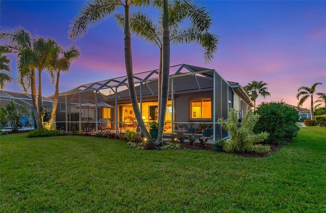 back house at dusk featuring a lanai and a yard