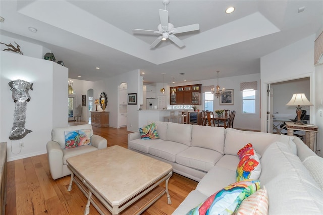 living room featuring a raised ceiling, light hardwood / wood-style flooring, and ceiling fan with notable chandelier