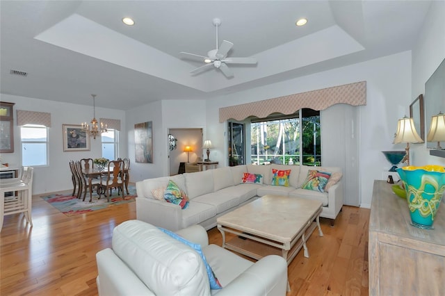 living room featuring plenty of natural light, light hardwood / wood-style floors, a raised ceiling, and ceiling fan with notable chandelier