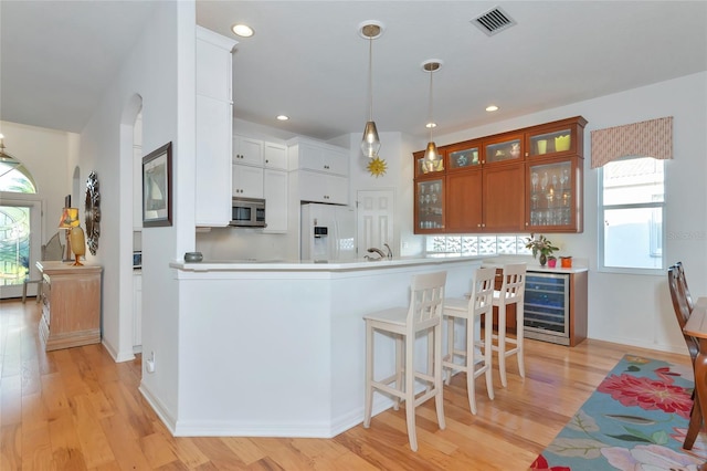 kitchen with light wood-type flooring, beverage cooler, pendant lighting, white cabinetry, and white fridge with ice dispenser