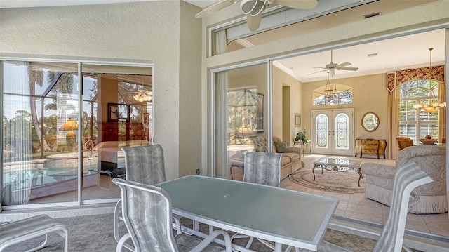 tiled dining space with french doors, crown molding, ceiling fan with notable chandelier, and a high ceiling