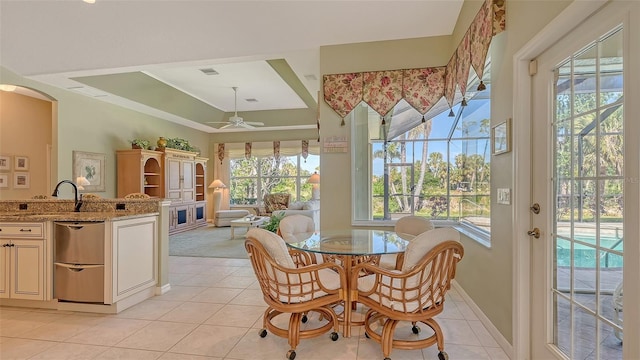 tiled dining area featuring ornamental molding, sink, ceiling fan, and a tray ceiling