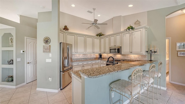 kitchen with light stone counters, stainless steel appliances, kitchen peninsula, and cream cabinets