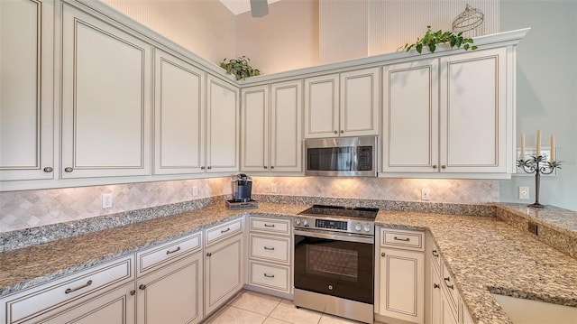 kitchen with stainless steel appliances, tasteful backsplash, cream cabinets, and light stone counters