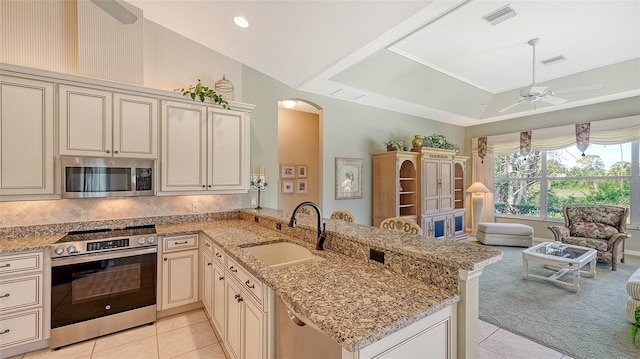 kitchen with sink, stainless steel appliances, light stone counters, cream cabinets, and kitchen peninsula