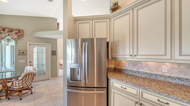 kitchen with stainless steel refrigerator with ice dispenser, light tile patterned flooring, stone counters, cream cabinets, and backsplash