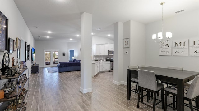 dining area with french doors, light hardwood / wood-style floors, and a notable chandelier