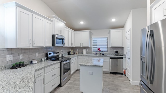 kitchen with a center island, white cabinets, sink, light stone counters, and stainless steel appliances