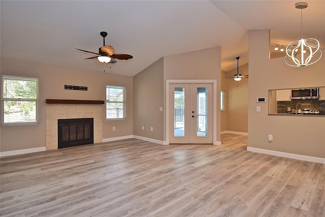 unfurnished living room with french doors, ceiling fan with notable chandelier, light hardwood / wood-style floors, a stone fireplace, and lofted ceiling