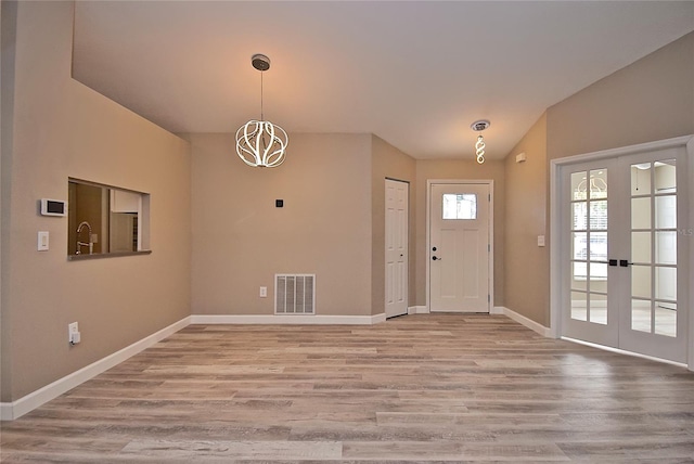 entrance foyer featuring french doors, vaulted ceiling, hardwood / wood-style flooring, and an inviting chandelier