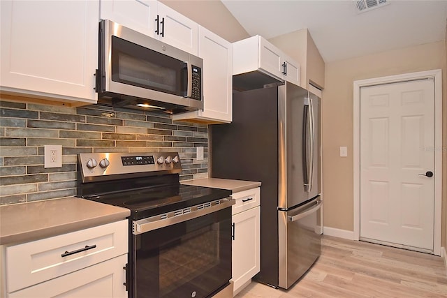 kitchen featuring white cabinetry, stainless steel appliances, light hardwood / wood-style flooring, vaulted ceiling, and decorative backsplash