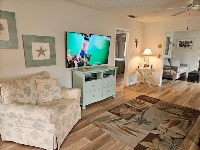 living room featuring ceiling fan, a textured ceiling, and hardwood / wood-style flooring