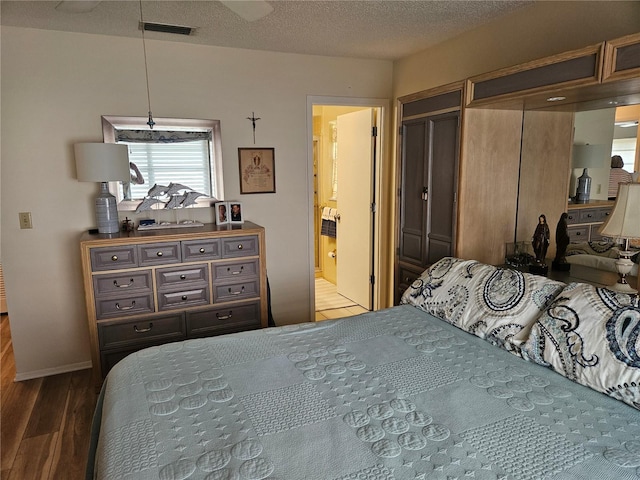 bedroom with hardwood / wood-style floors, a textured ceiling, connected bathroom, and a closet