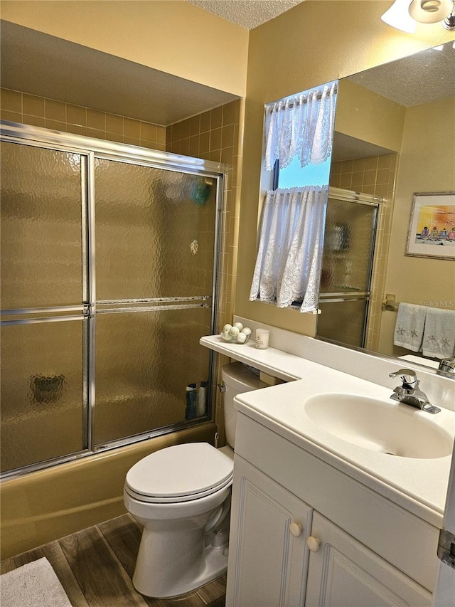 full bathroom with combined bath / shower with glass door, a textured ceiling, vanity, hardwood / wood-style flooring, and toilet