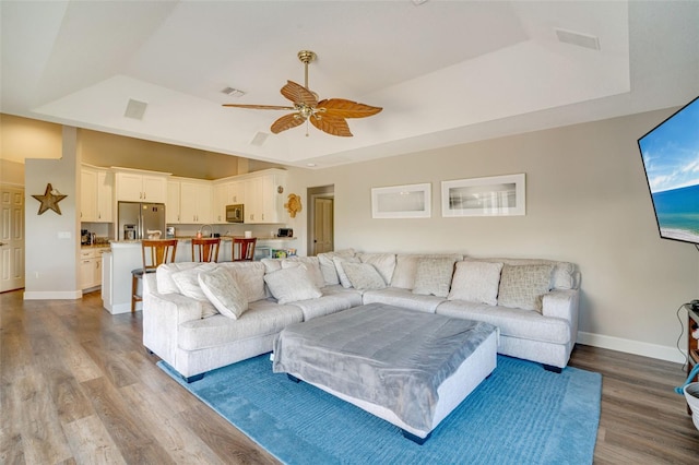 living room with ceiling fan, a raised ceiling, and light hardwood / wood-style flooring