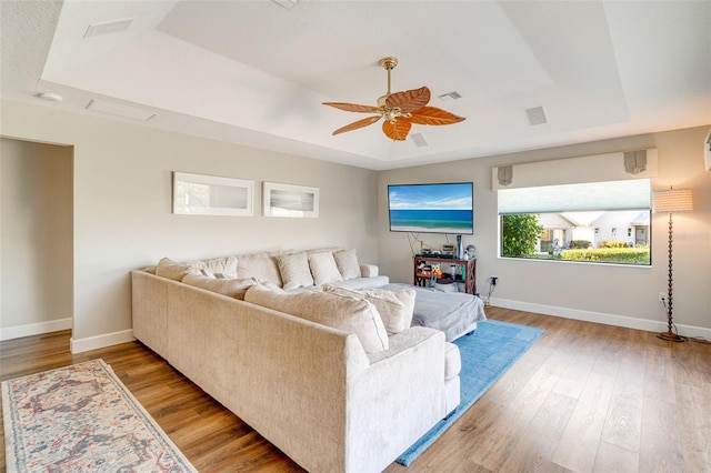 living room featuring ceiling fan, a raised ceiling, and light hardwood / wood-style flooring