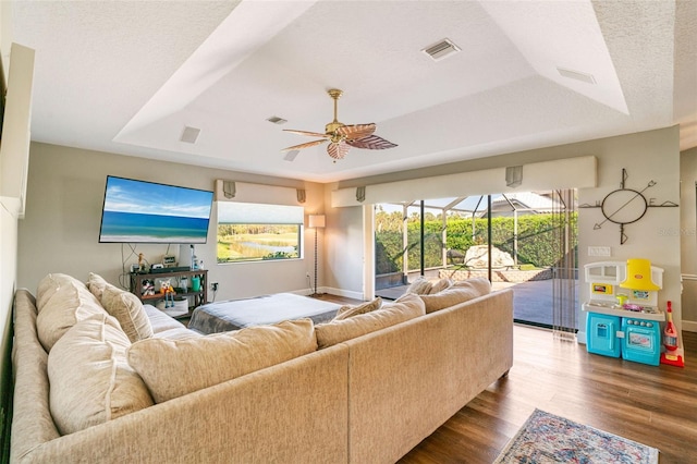 living room featuring hardwood / wood-style flooring, ceiling fan, a textured ceiling, and a tray ceiling