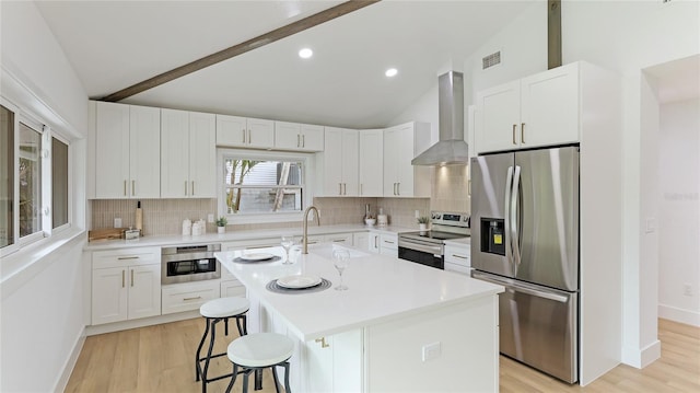 kitchen featuring a kitchen island with sink, vaulted ceiling with beams, stainless steel appliances, a kitchen breakfast bar, and wall chimney exhaust hood