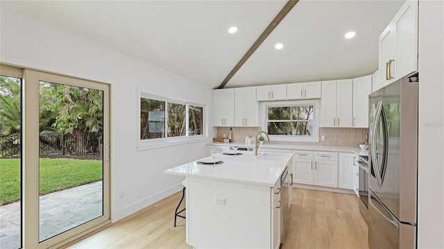 kitchen with appliances with stainless steel finishes, a kitchen island with sink, a kitchen breakfast bar, white cabinets, and decorative backsplash