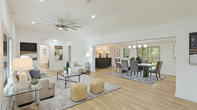 living area with vaulted ceiling, ceiling fan with notable chandelier, light wood-style flooring, baseboards, and visible vents