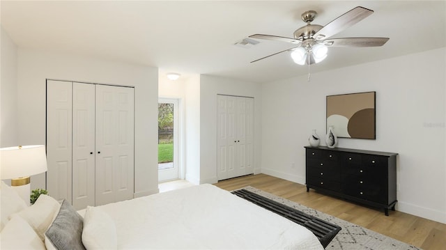 bedroom with light wood-type flooring, a ceiling fan, baseboards, and two closets
