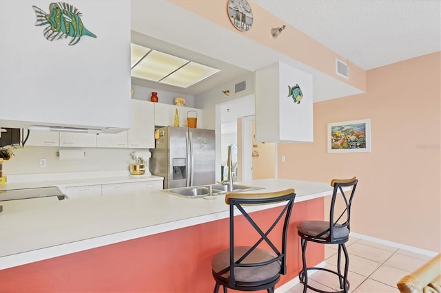 kitchen with white cabinetry, stainless steel refrigerator with ice dispenser, kitchen peninsula, a breakfast bar, and light tile patterned floors