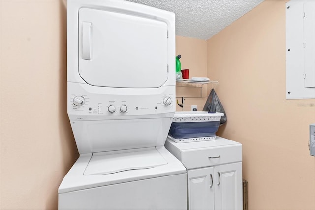 washroom with a textured ceiling, electric panel, cabinets, and stacked washer / drying machine