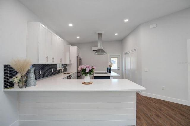 kitchen with kitchen peninsula, sink, white cabinetry, and wall chimney range hood