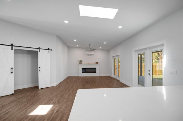 unfurnished living room featuring hardwood / wood-style floors, ceiling fan, a barn door, and a skylight