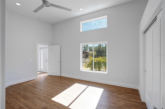 unfurnished bedroom with a closet, a towering ceiling, dark hardwood / wood-style floors, and ceiling fan