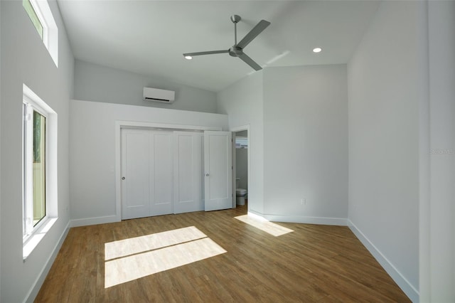 unfurnished bedroom featuring a wall unit AC, multiple windows, ceiling fan, and hardwood / wood-style floors