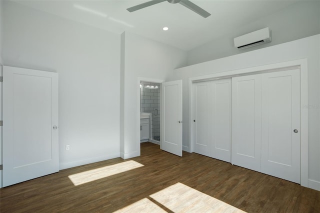 unfurnished bedroom with a wall mounted air conditioner, dark hardwood / wood-style flooring, ceiling fan, connected bathroom, and a closet