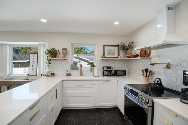 kitchen featuring sink, white cabinets, stainless steel range with electric cooktop, backsplash, and wall chimney range hood