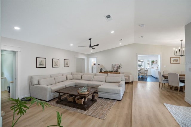 living room featuring vaulted ceiling, ceiling fan with notable chandelier, and light wood-type flooring