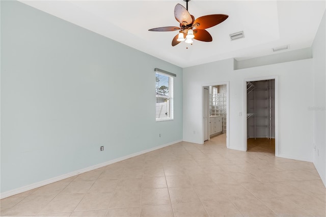 unfurnished bedroom featuring ceiling fan, ensuite bath, a spacious closet, light tile patterned floors, and a closet