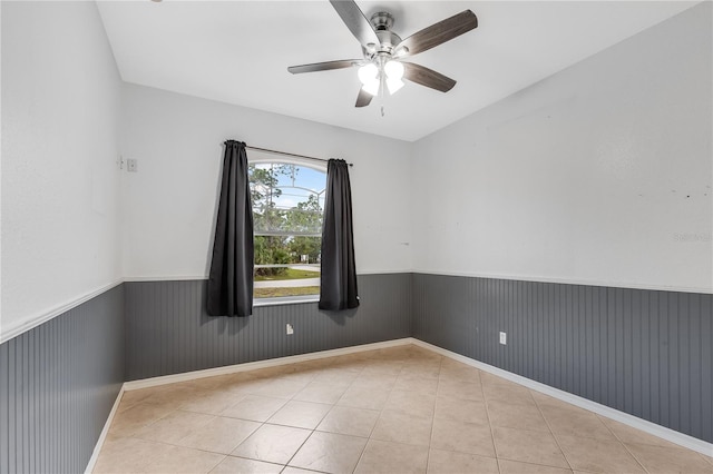 tiled empty room featuring ceiling fan and wooden walls