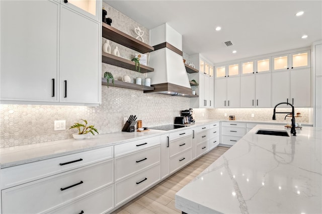 kitchen with light stone countertops, backsplash, black electric cooktop, sink, and white cabinetry