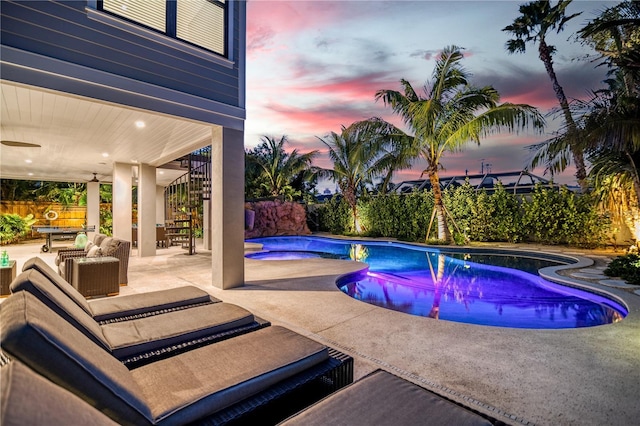 pool at dusk featuring outdoor lounge area, a patio, and a hot tub