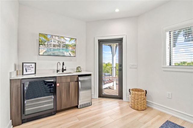 bar with sink, refrigerator, beverage cooler, and light hardwood / wood-style flooring