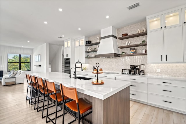 kitchen featuring white cabinets, custom range hood, a kitchen island with sink, and sink