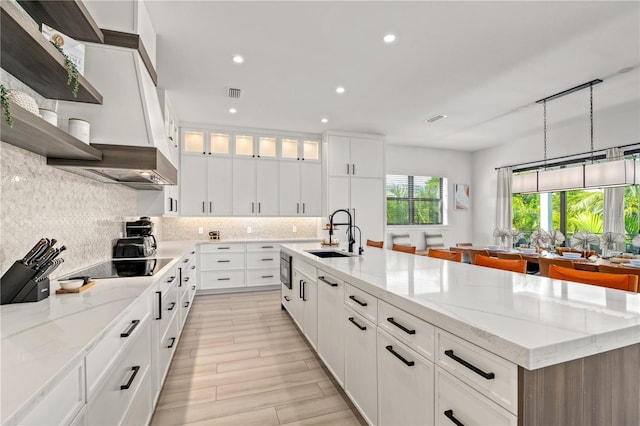 kitchen featuring white cabinets, sink, an island with sink, and black electric cooktop