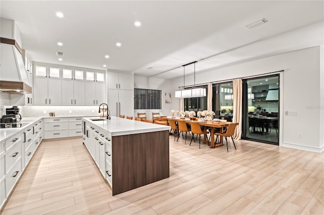 kitchen with sink, white cabinets, light hardwood / wood-style floors, hanging light fixtures, and an island with sink