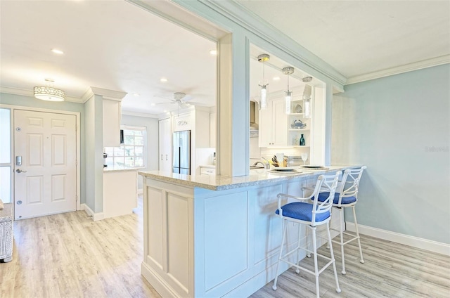 kitchen featuring kitchen peninsula, light wood-type flooring, decorative light fixtures, white cabinets, and stainless steel refrigerator