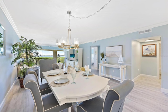 dining area featuring light wood-type flooring, an inviting chandelier, and crown molding