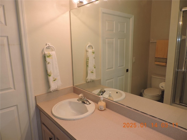 bathroom featuring a shower with shower door, vanity, and toilet