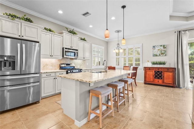 kitchen featuring white cabinetry, sink, stainless steel appliances, light stone counters, and a center island with sink