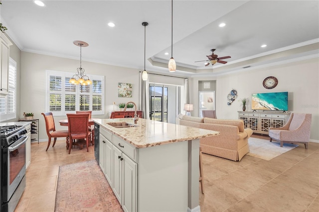 kitchen featuring a kitchen island with sink, a raised ceiling, stainless steel range with gas cooktop, sink, and white cabinetry