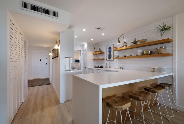 kitchen with white cabinets, a kitchen breakfast bar, sink, light wood-type flooring, and kitchen peninsula